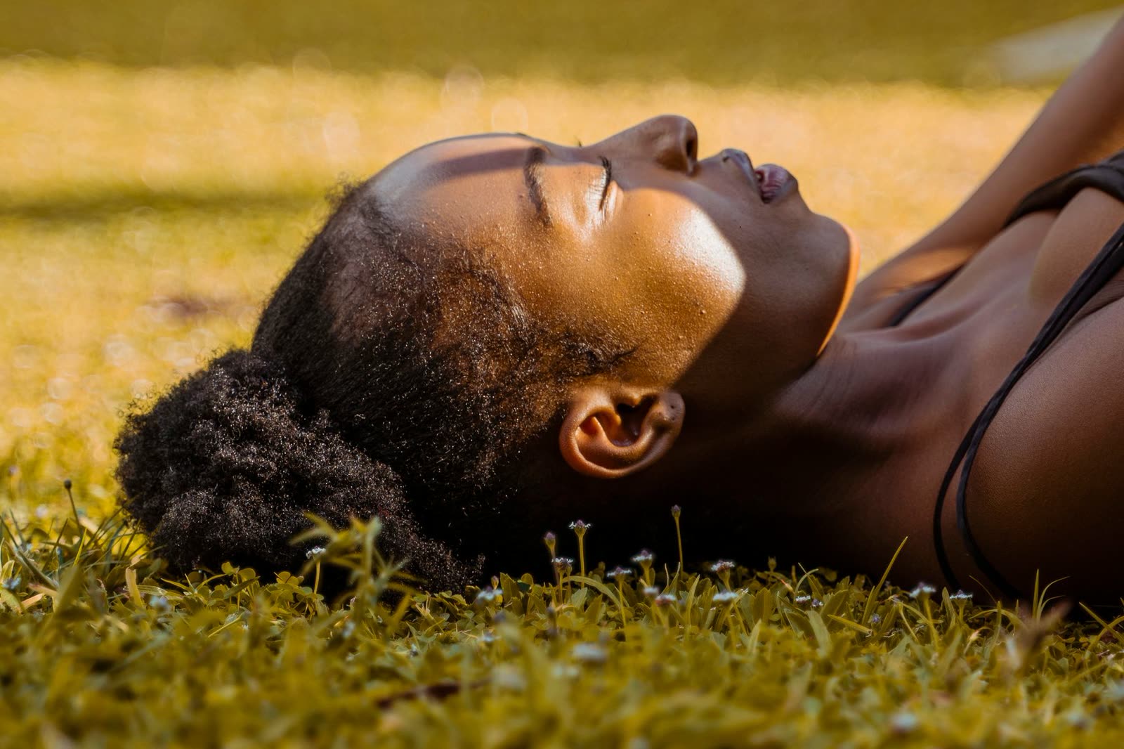 A woman lying on the grass in warm sunlight, eyes closed
